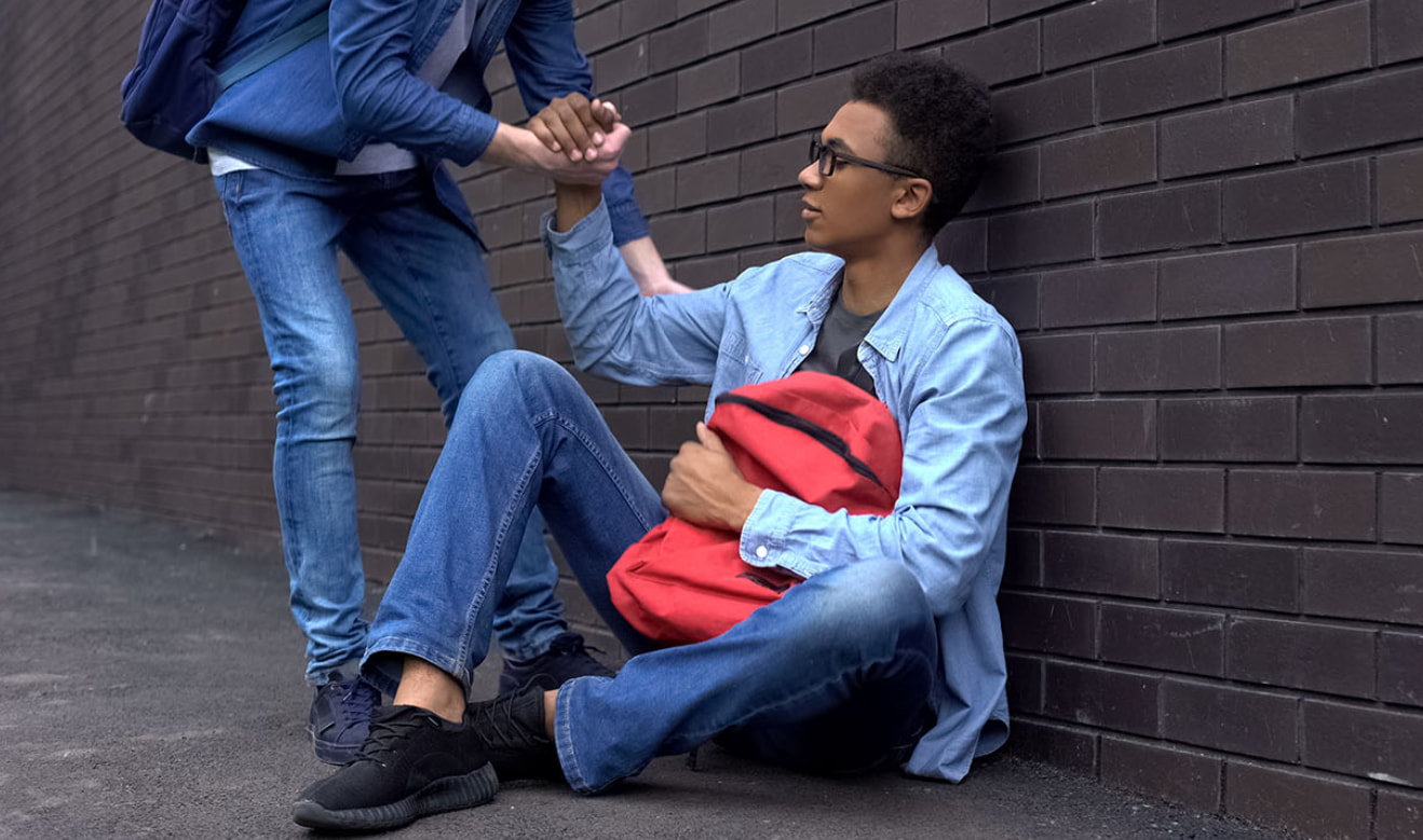 Two young men sitting on the ground, hands resting on each other, sharing a moment of connection and friendship.