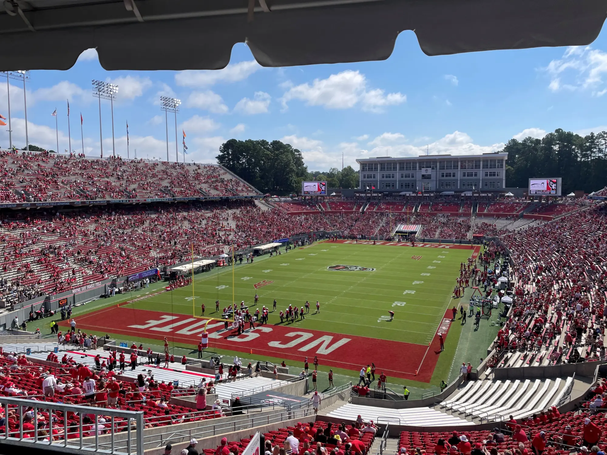 NC State football stadium filled with fans wearing red on a sunny day, view from upper seating overlooking the field and end zone.