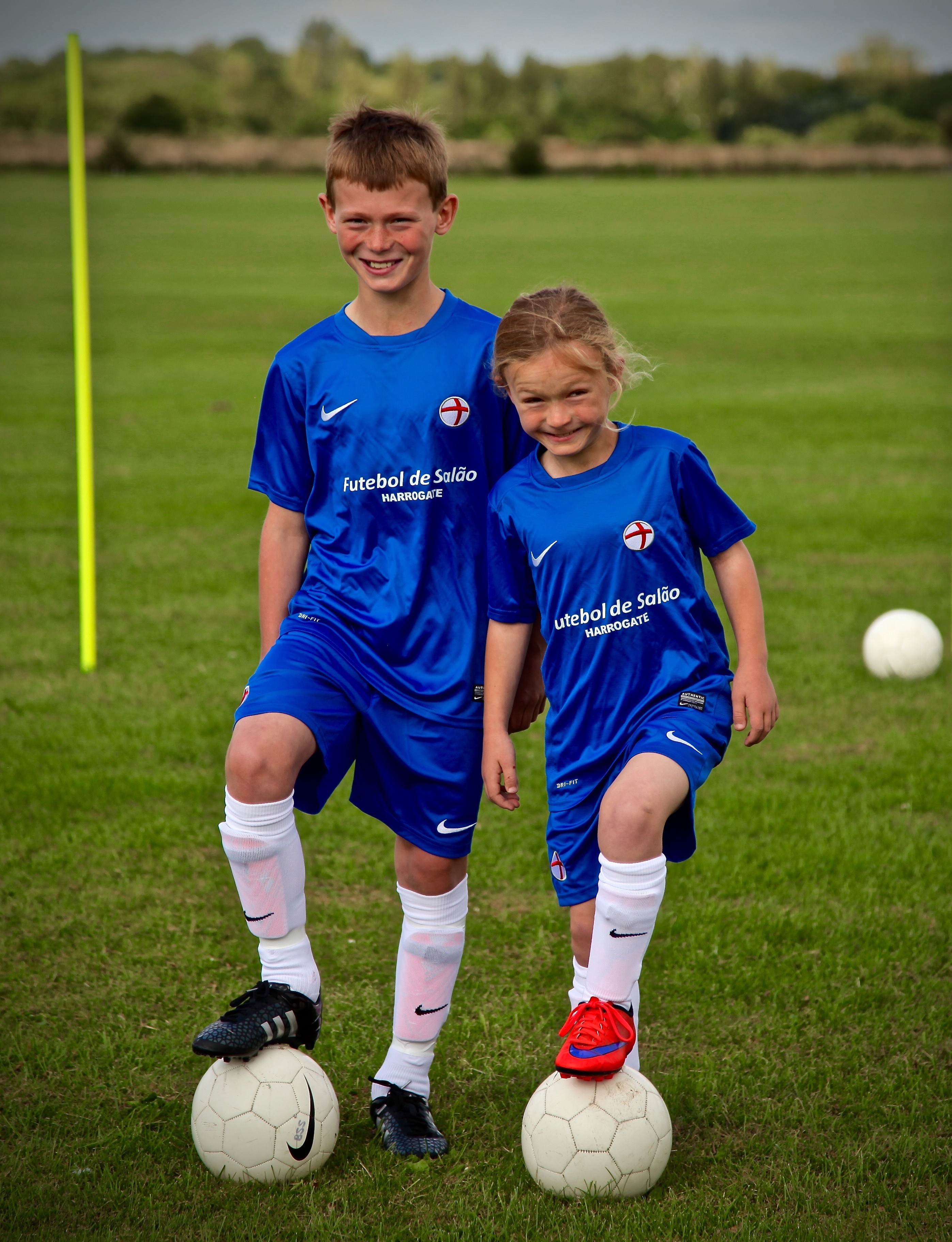 Young girl in black sportswear skillfully controlling a soccer ball mid-air indoors with an audience watching behind a blue barrier.