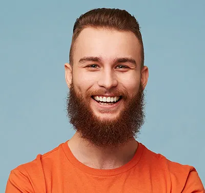 Junger Mann mit rotem Bart und orangenem T-Shirt lächelt vor blauem Hintergrund.