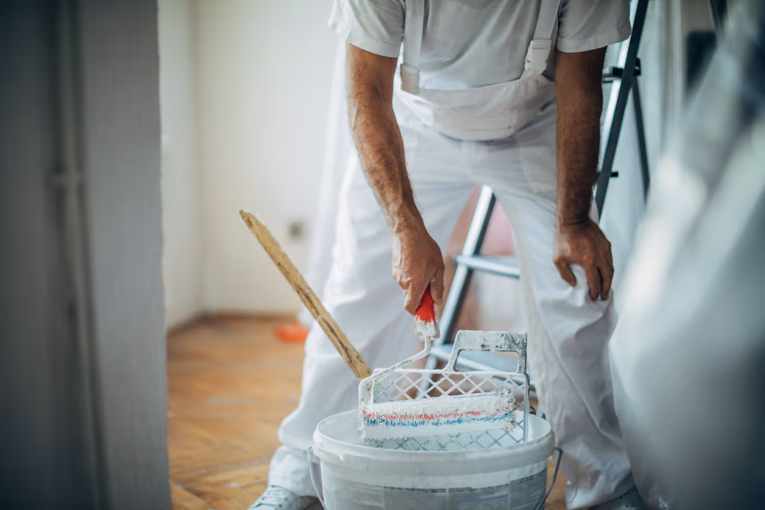 Maler in weißer Arbeitskleidung taucht Farbroller in Farbeimer während Renovierung.