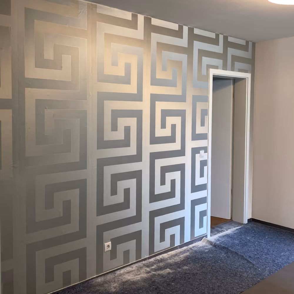 Raum mit einer Wand, die mit geometrischem tapetenmuster in Grau- und Beigetönen dekoriert ist, mit einer offenen Tür rechts.