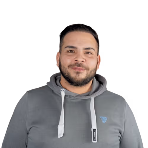 Porträt eines lächelnden Mannes mit kurzem Bart in einem grauen Kapuzenpullover vor schwarzem Hintergrund.