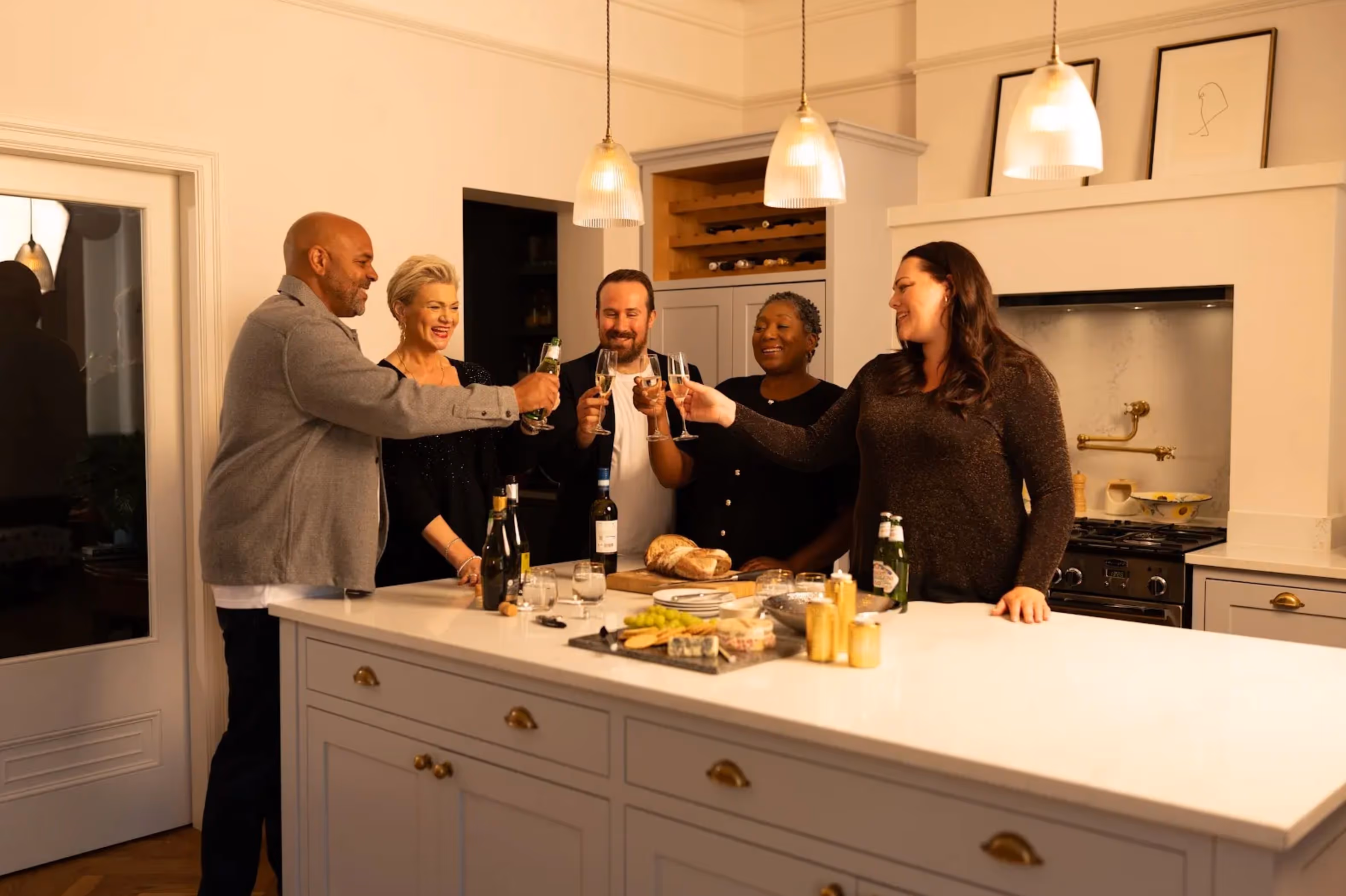 Five people toasting drinks around a kitchen island during a festive dinner, promoting CheqUp’s Season’s Eatings campaign.