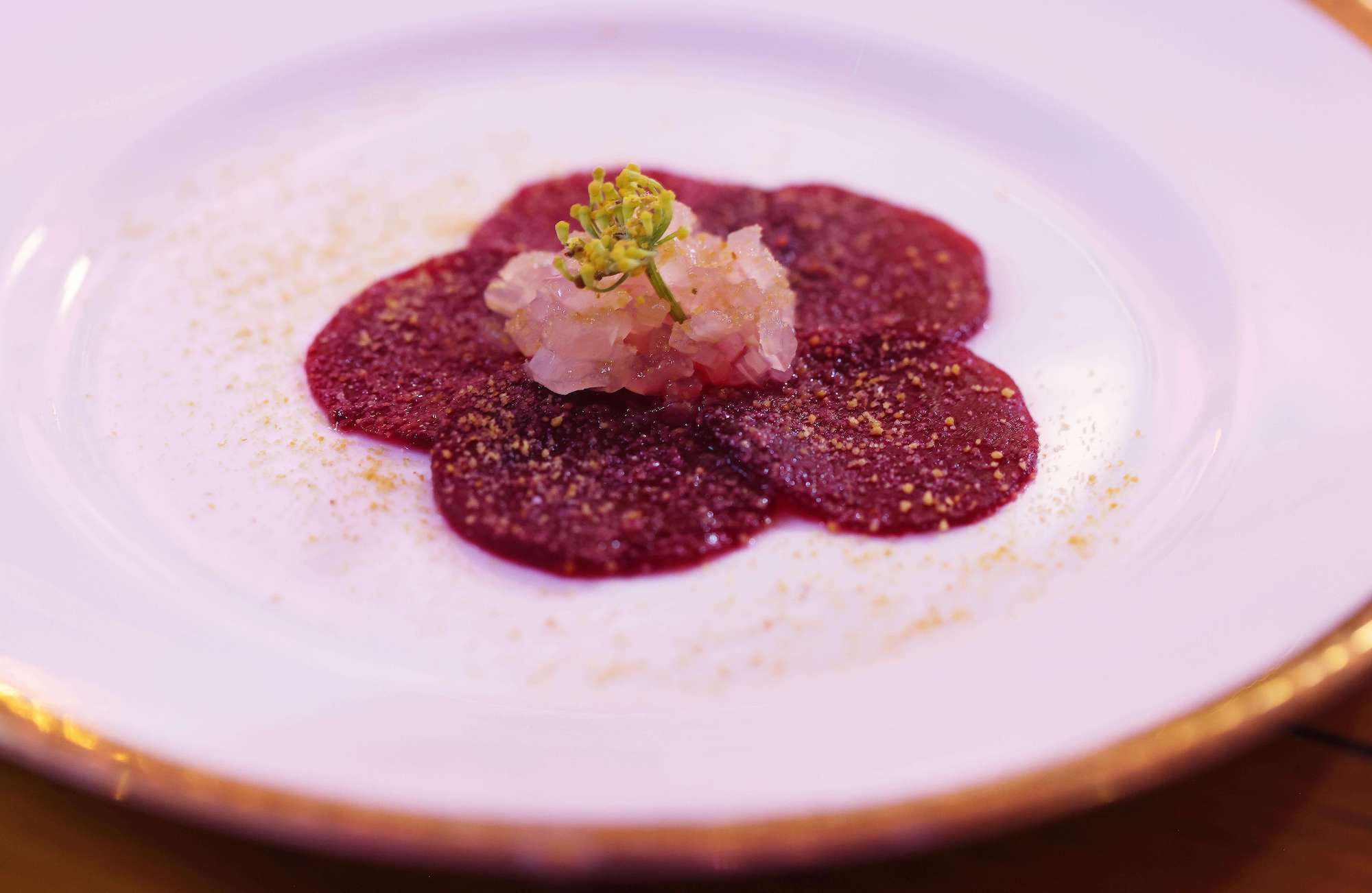 Beetroot carpaccio with shallots and herbs by Jack Stein on white plate with gold rim