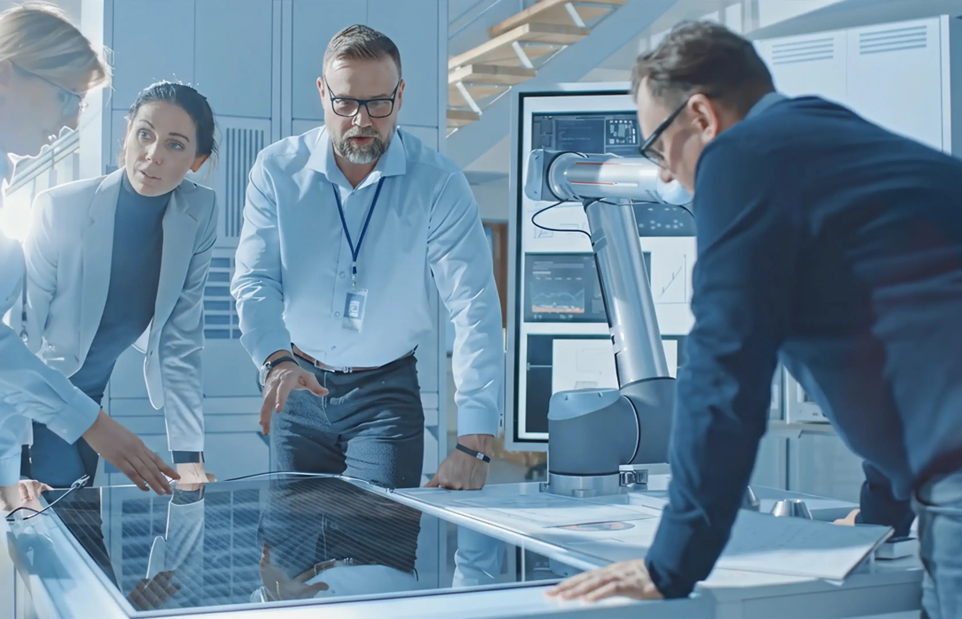 Four medial professionals collaborating around a digital table with robotic arm and technical screens in a modern lab.