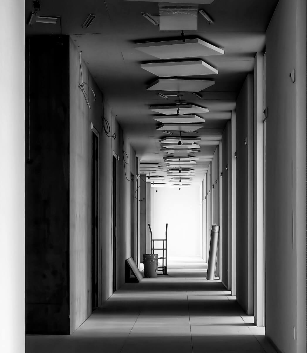Long indoor corridor under construction with suspended ceiling panels, a hand truck, and construction materials.