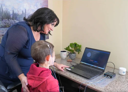 "Dr. Roseann Capanna-Hodge guiding a young child through a neurofeedback session, with the child seated calmly wearing EEG sensors, illustrating a gentle and supportive approach to brain-based therapy in a clinical setting.