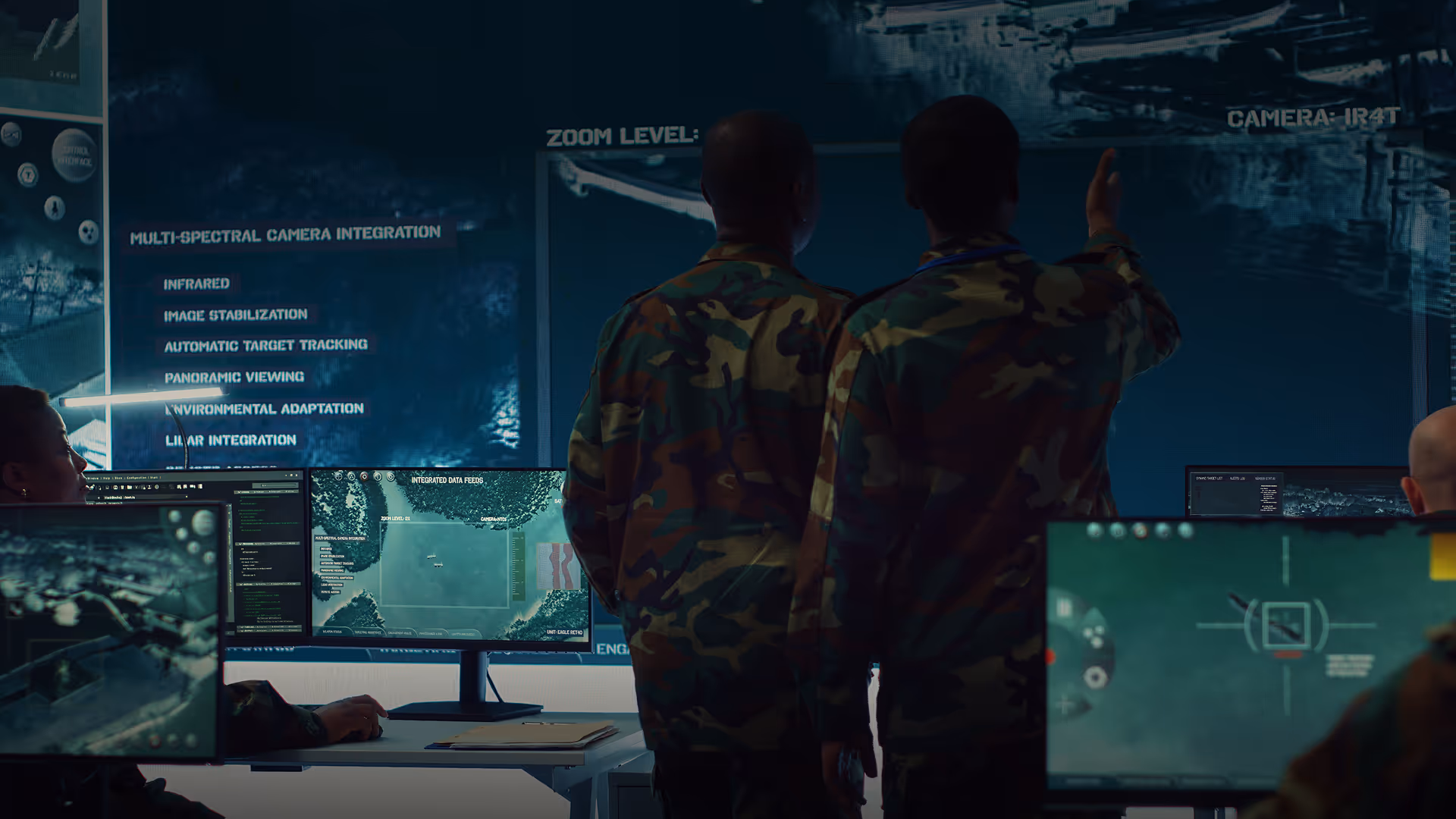 Military personnel in camouflage uniforms analyzing data on multiple computer screens with surveillance and mapping information.