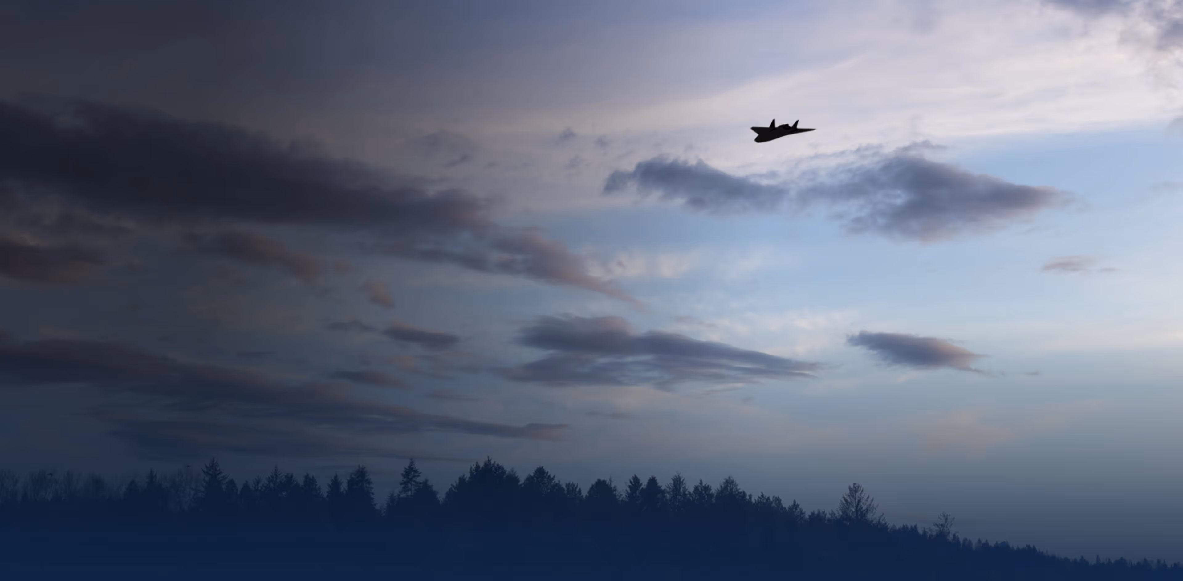 Silhouette of a UAV Tracer flying above a tree line under a cloudy sky at dusk.