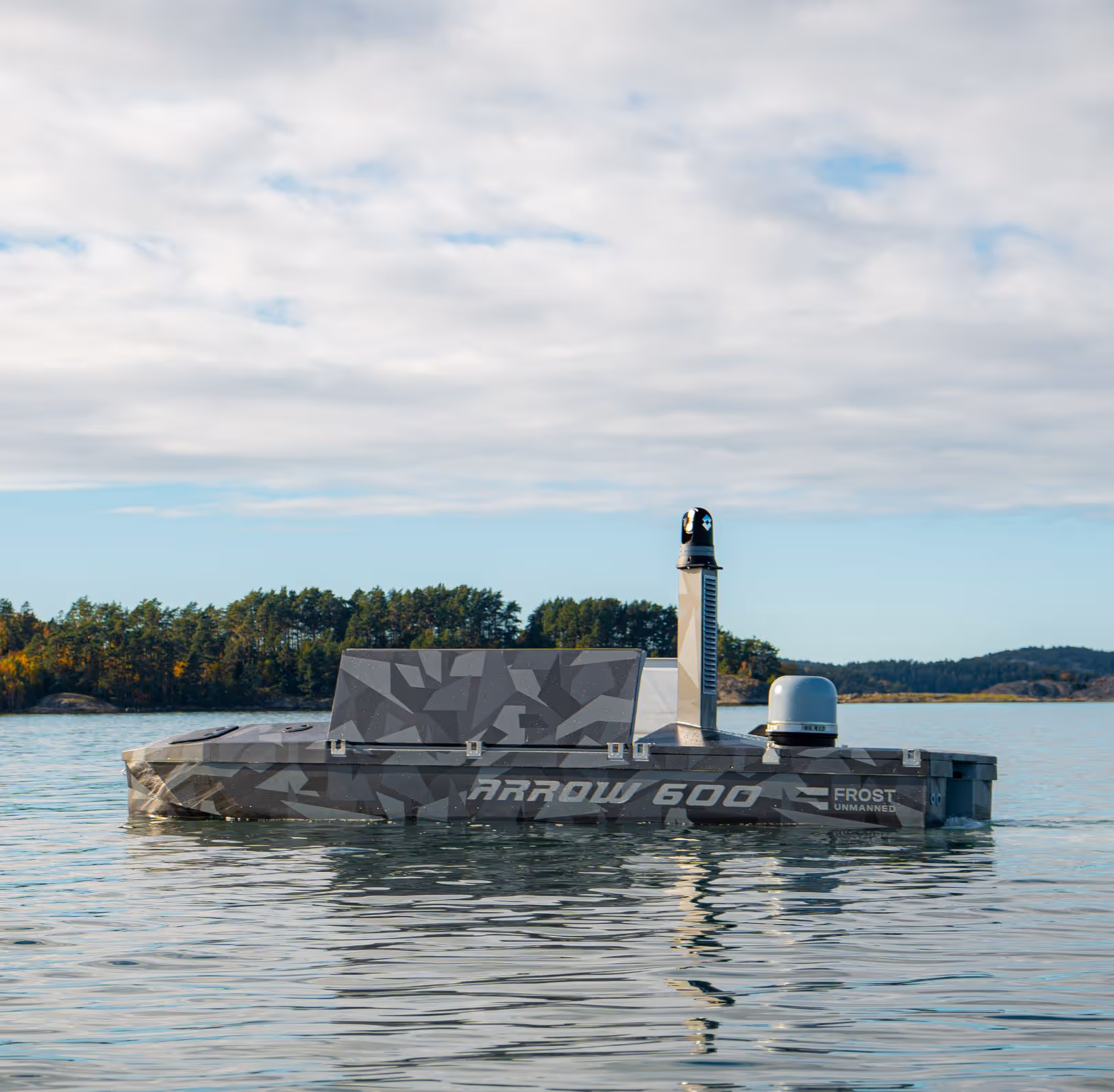 Camouflaged unmanned surface vessel labeled Arrow 600 floating on calm water near a tree-lined shore.