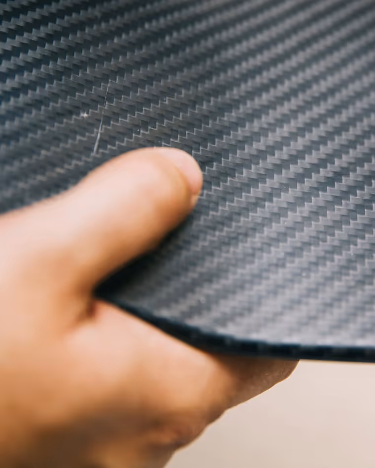 Close-up of a hand holding a dark carbon fiber patterned surface with a visible scratch.