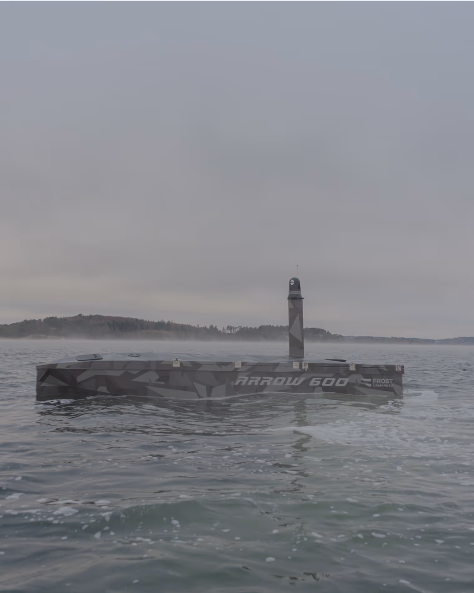Camouflaged autonomous surface vessel labeled Arrow 600 on calm water under a cloudy sky with distant shoreline.