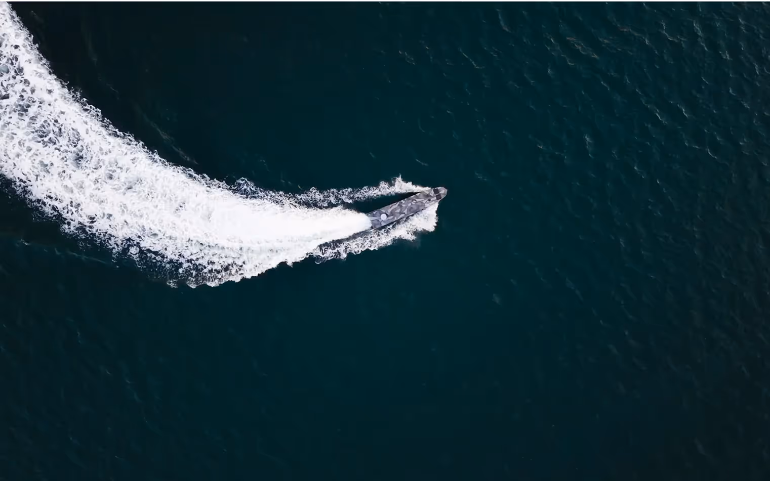 A USV making a sharp turn, leaving a white wake trail on dark blue water, viewed from above.