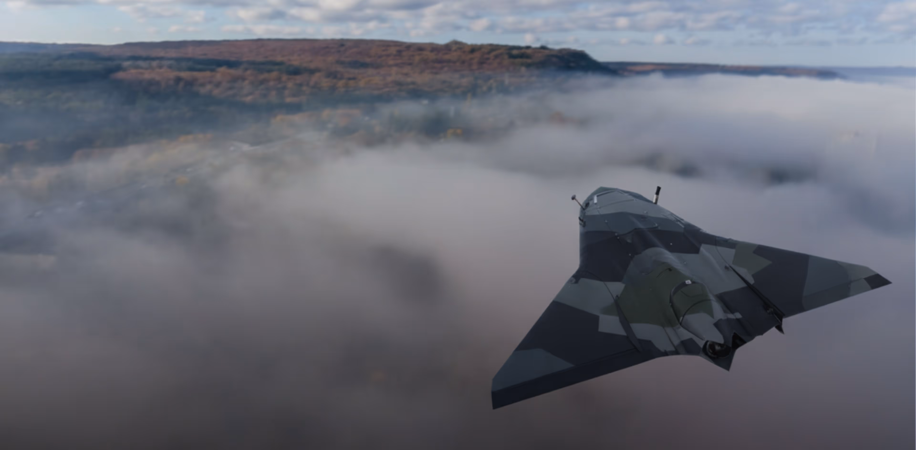 Camouflage military drone flying above clouds with forested hills in the background.