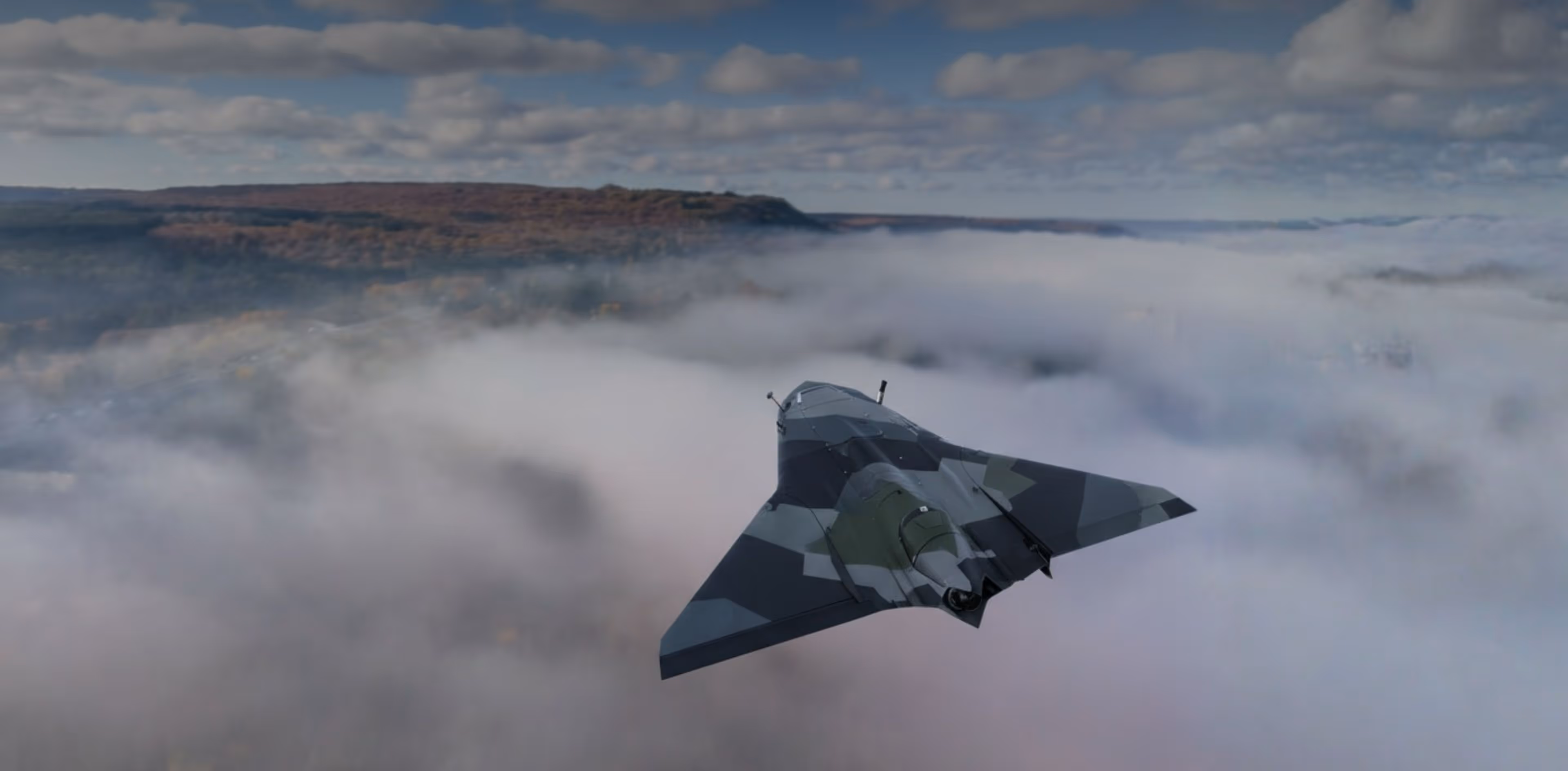 A military stealth UAV flying above thick clouds with a mountainous landscape in the distance.