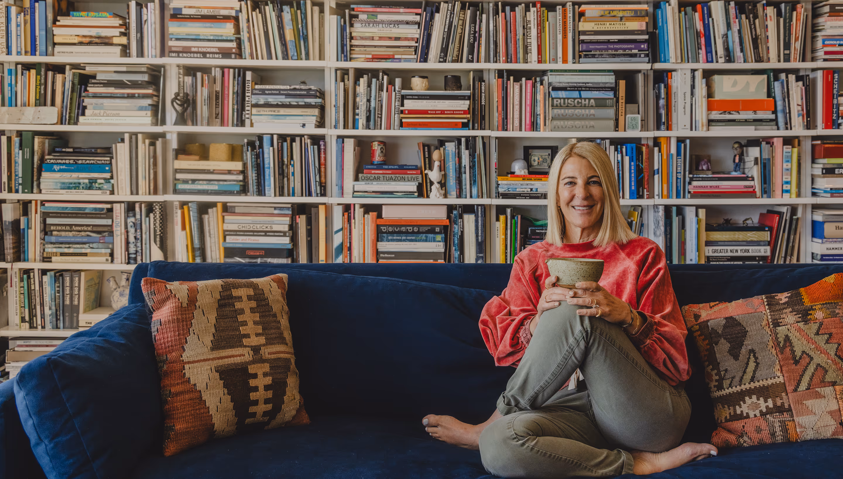 Heidi sitting on a couch with a ceramic cup and book shelves in the background