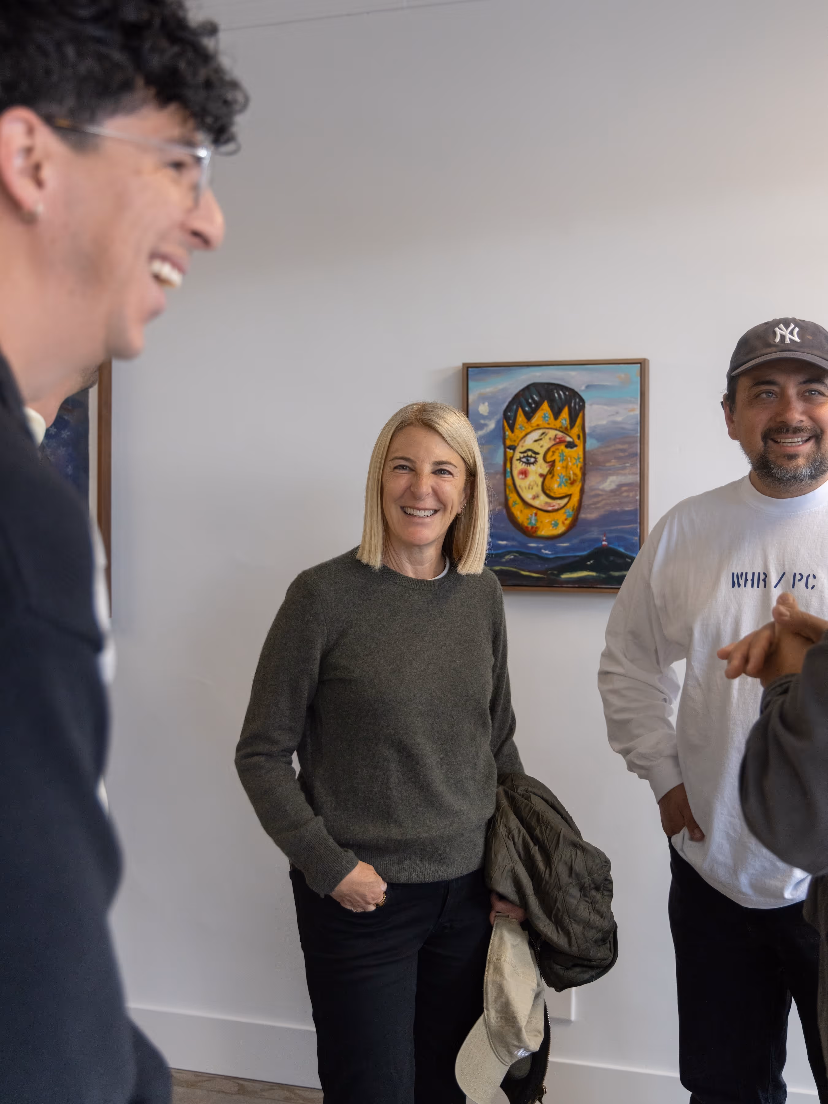 Three people chatting and smiling in an art gallery. 