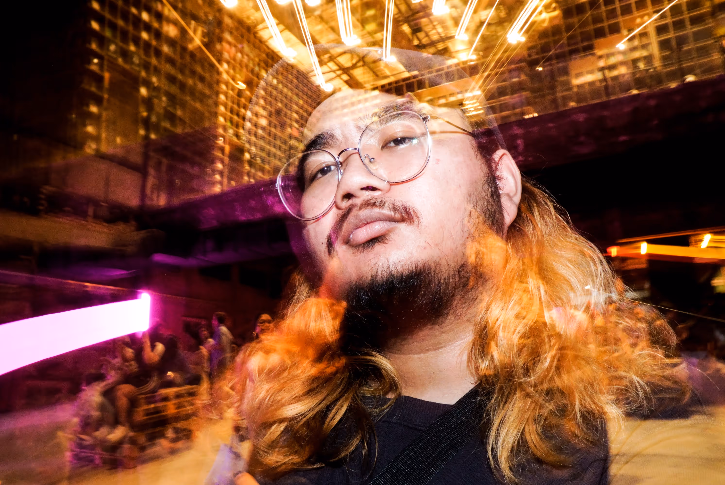 ChatGPT said:  A photo of a man with long hair and glasses posing confidently at a vibrant nightlife event, captured by Silver Star Pro — emphasizing creative event photography and videography in Dubai with artistic motion blur and colorful lighting.