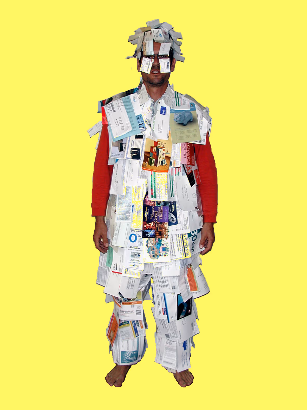 Man wearing a suit covered entirely with various paper documents and cards, standing barefoot against a yellow background.