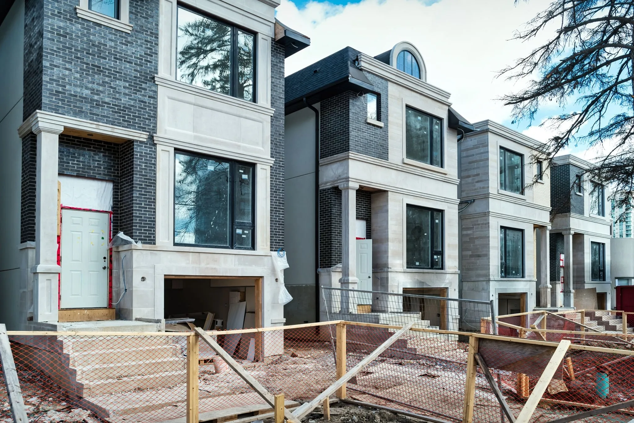 Row of modern townhouses under construction with unfinished garages, stairs, and protective orange fencing.