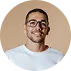 Smiling man with short hair, glasses, and a white shirt against a beige background.