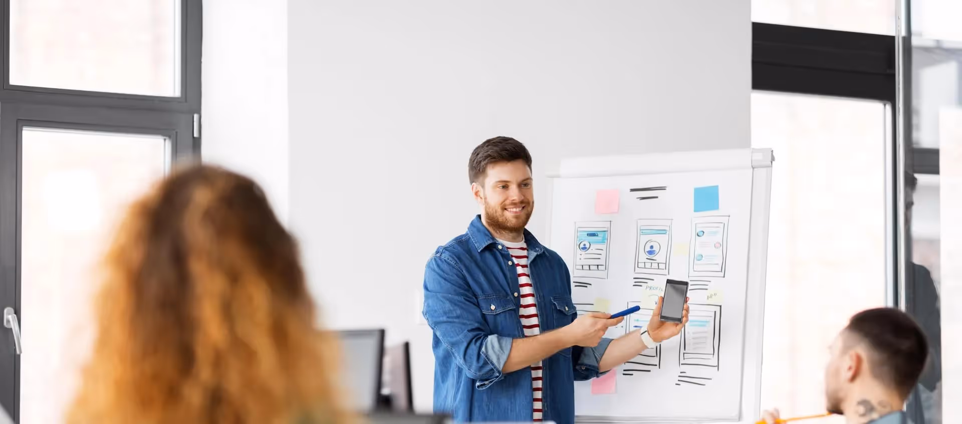 Young man presenting app wireframes on a whiteboard to colleagues in a bright office