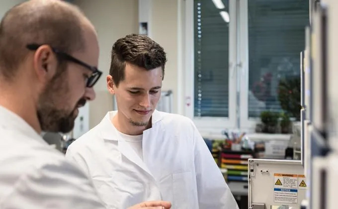 Two men in white lab coats working at a laboratory instrument