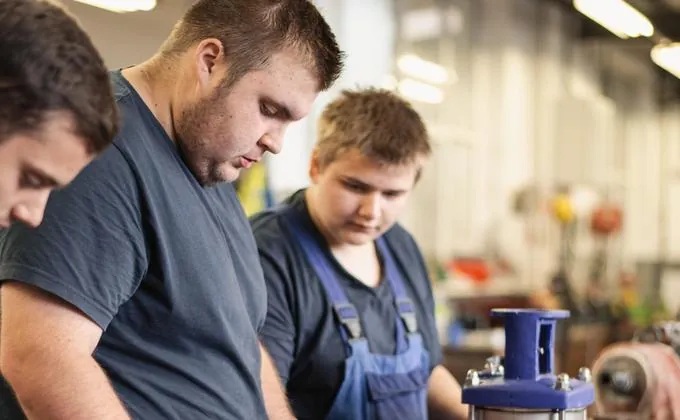 Three young apprentices in work clothes concentrating on a metal part in a workshop