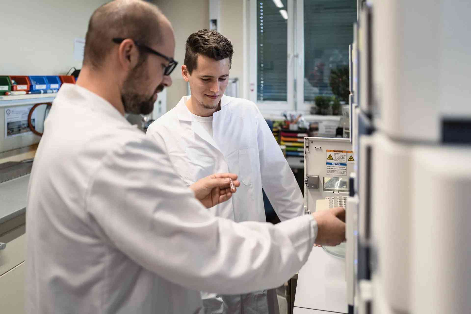 Two lab technicians in white coats operating an analysis device at the AGRANA plant in Aschach