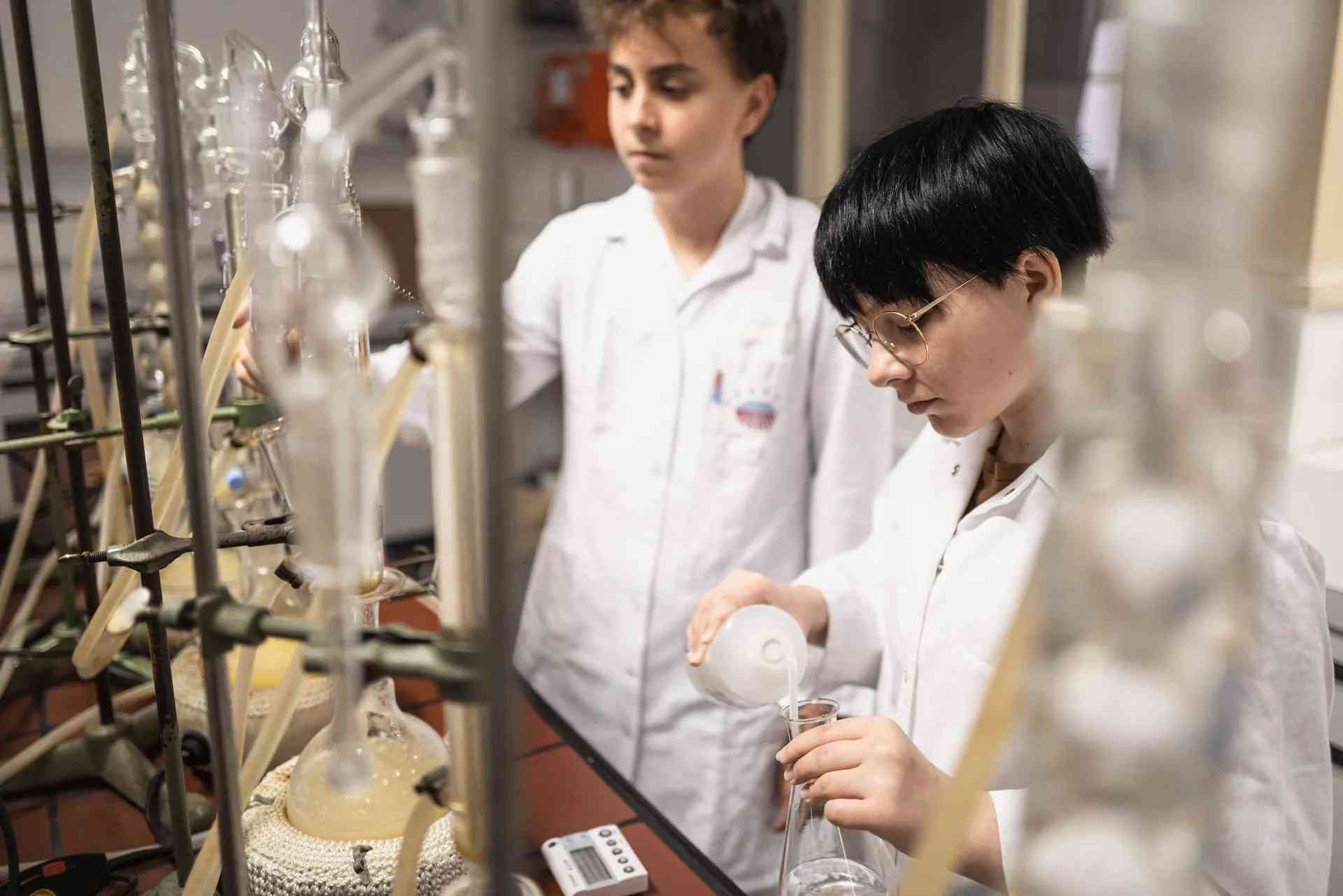 Two young lab technicians in white coats working with glass apparatus at the AGRANA plant in Gmünd