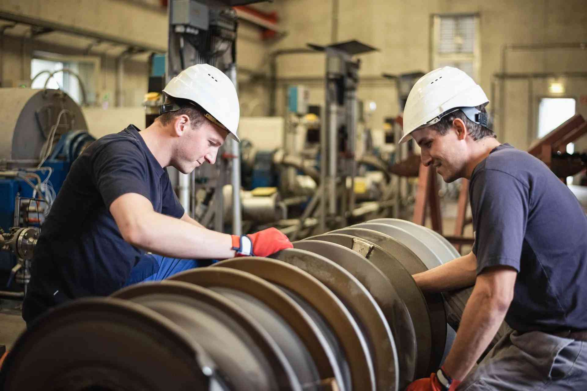 Two workers in hard hats inspecting a large steel screw shaft in an AGRANA workshop in Pischelsdorf