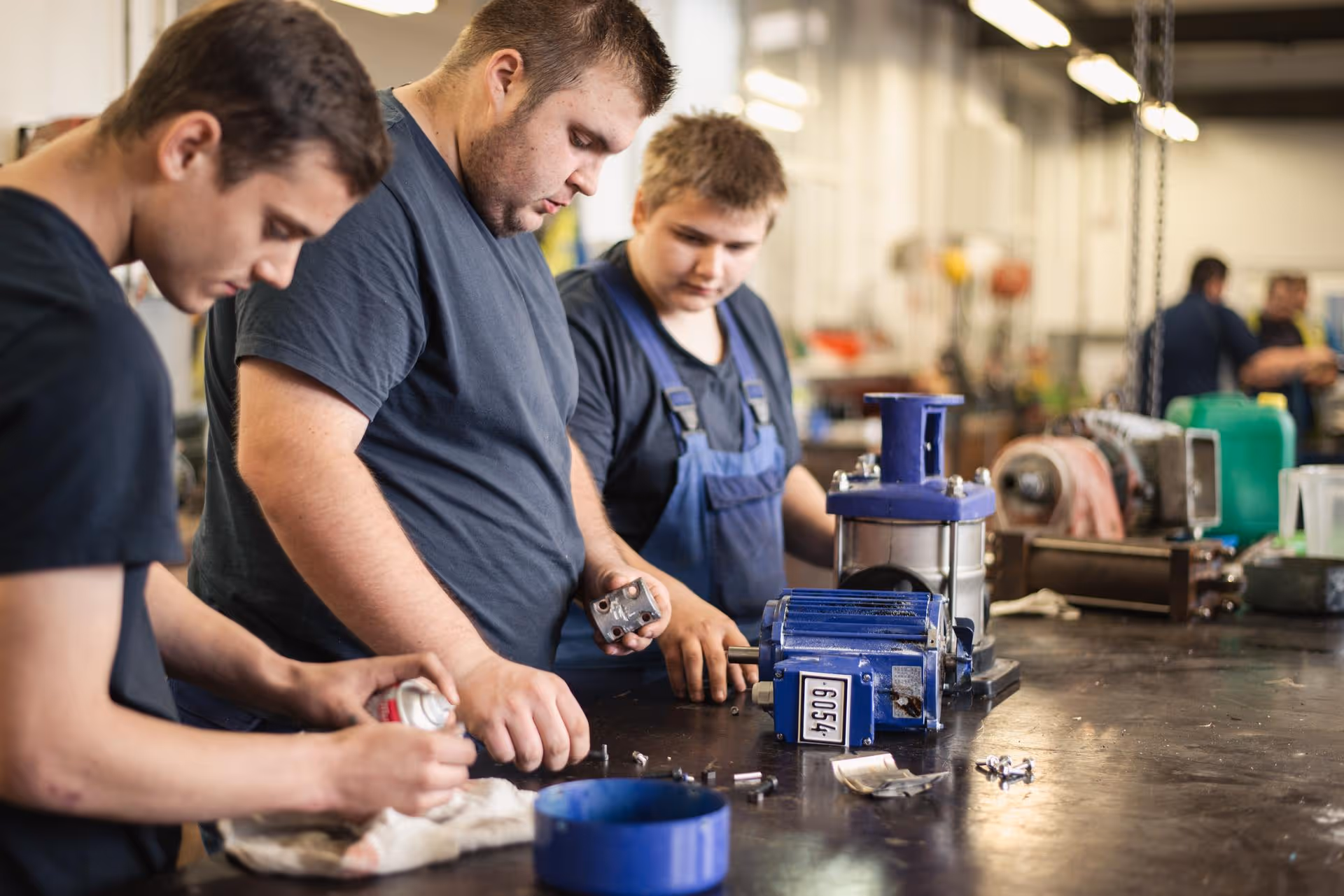 Three apprentices in work clothes assembling metal parts at a workbench in the AGRANA workshop in Gmünd