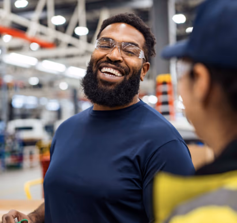 Laughing worker in safety glasses talking to a colleague in a production hall