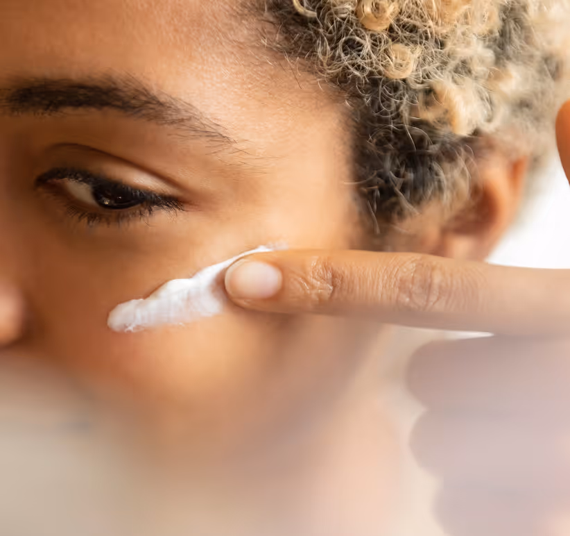 Close-up of a woman applying a stroke of white face cream under her eye