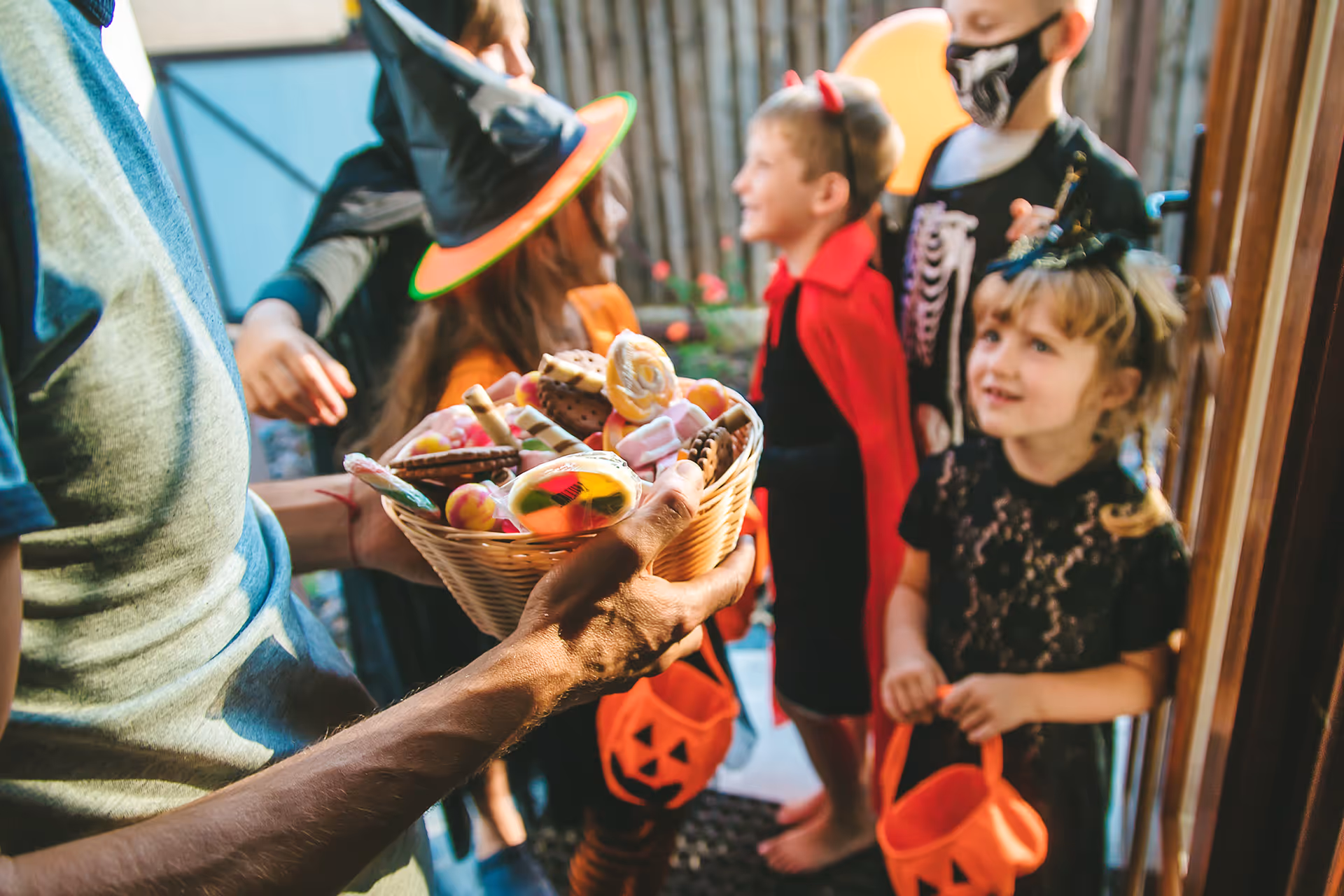 Erwachsener reicht Kindern in Halloween-Kostümen an der Haustür einen Korb voller Süßigkeiten [no AI]