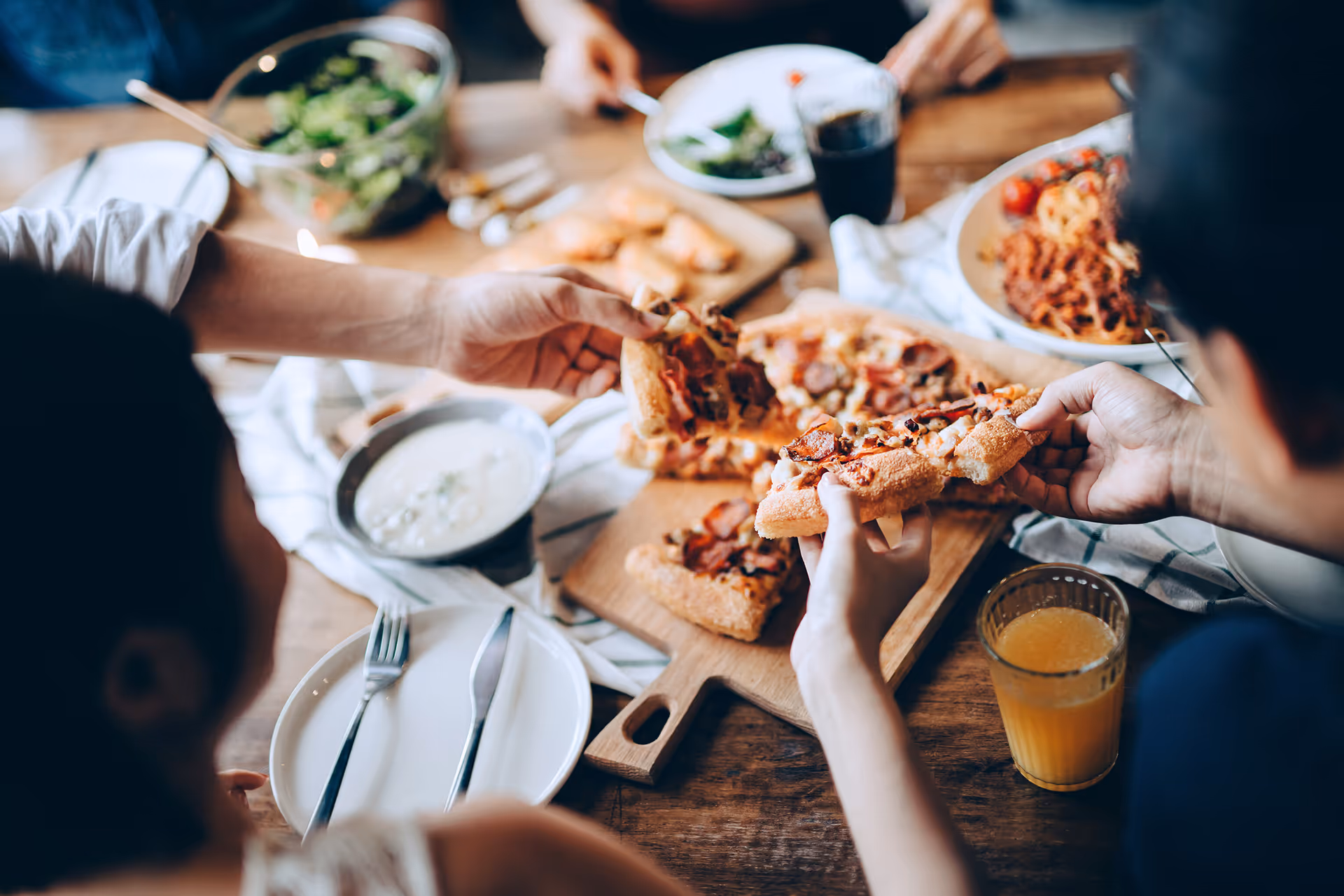 Freunde teilen Pizzastücke, Salat und Getränke an einem hölzernen Esstisch