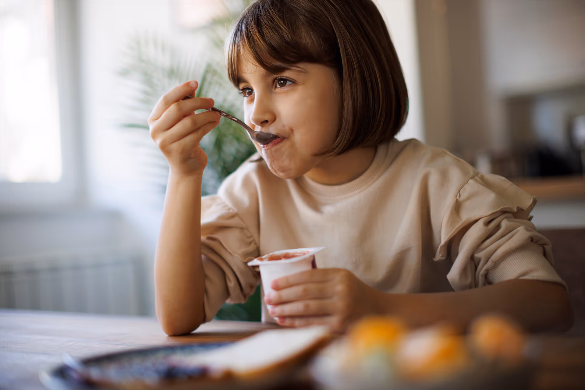 Mädchen löffelt am Küchentisch Joghurt aus einem Becher [no AI]