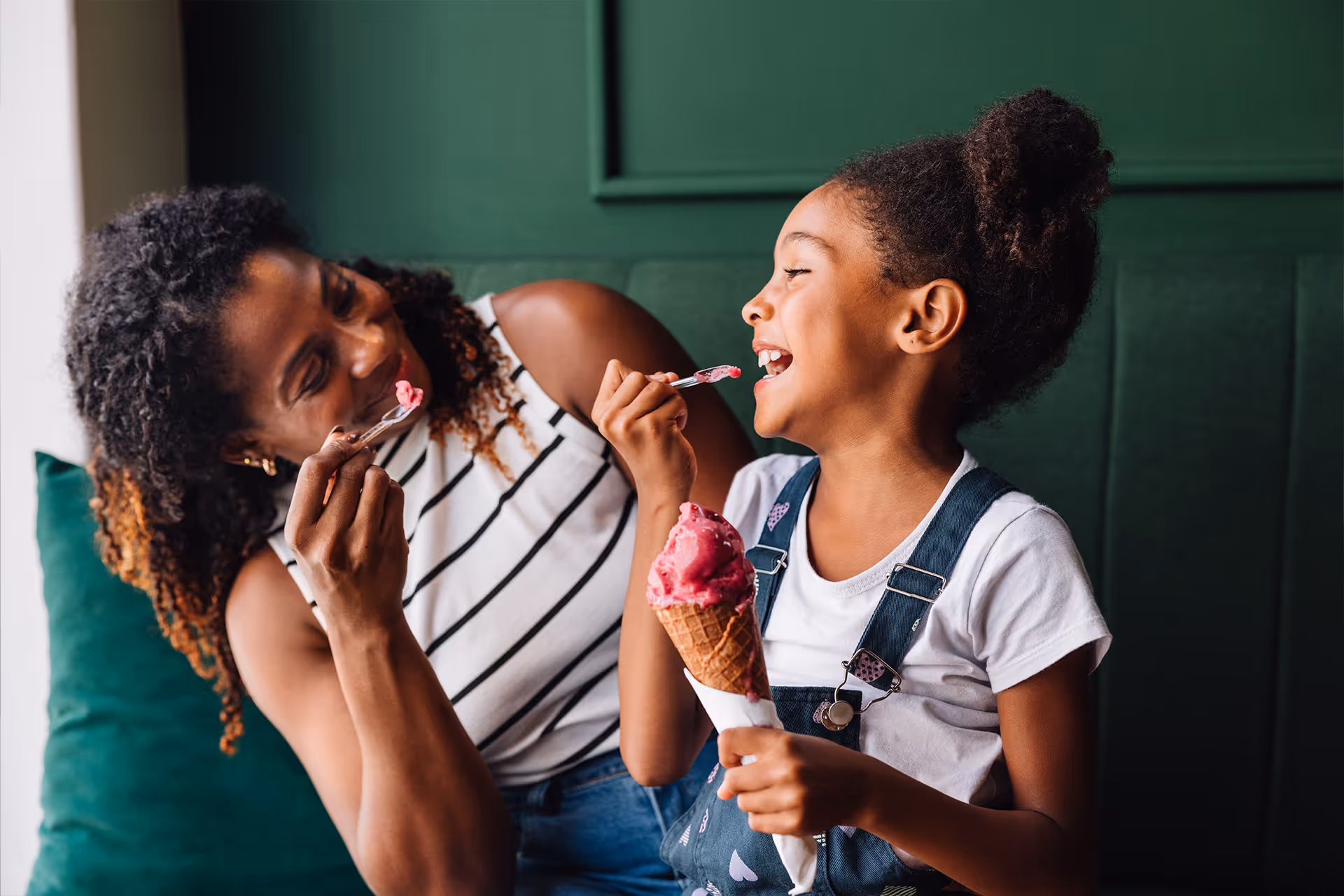 Mutter und Tochter lachen und teilen sich ein rosa Eis in der Waffel auf einem grünen Sofa [no AI]
