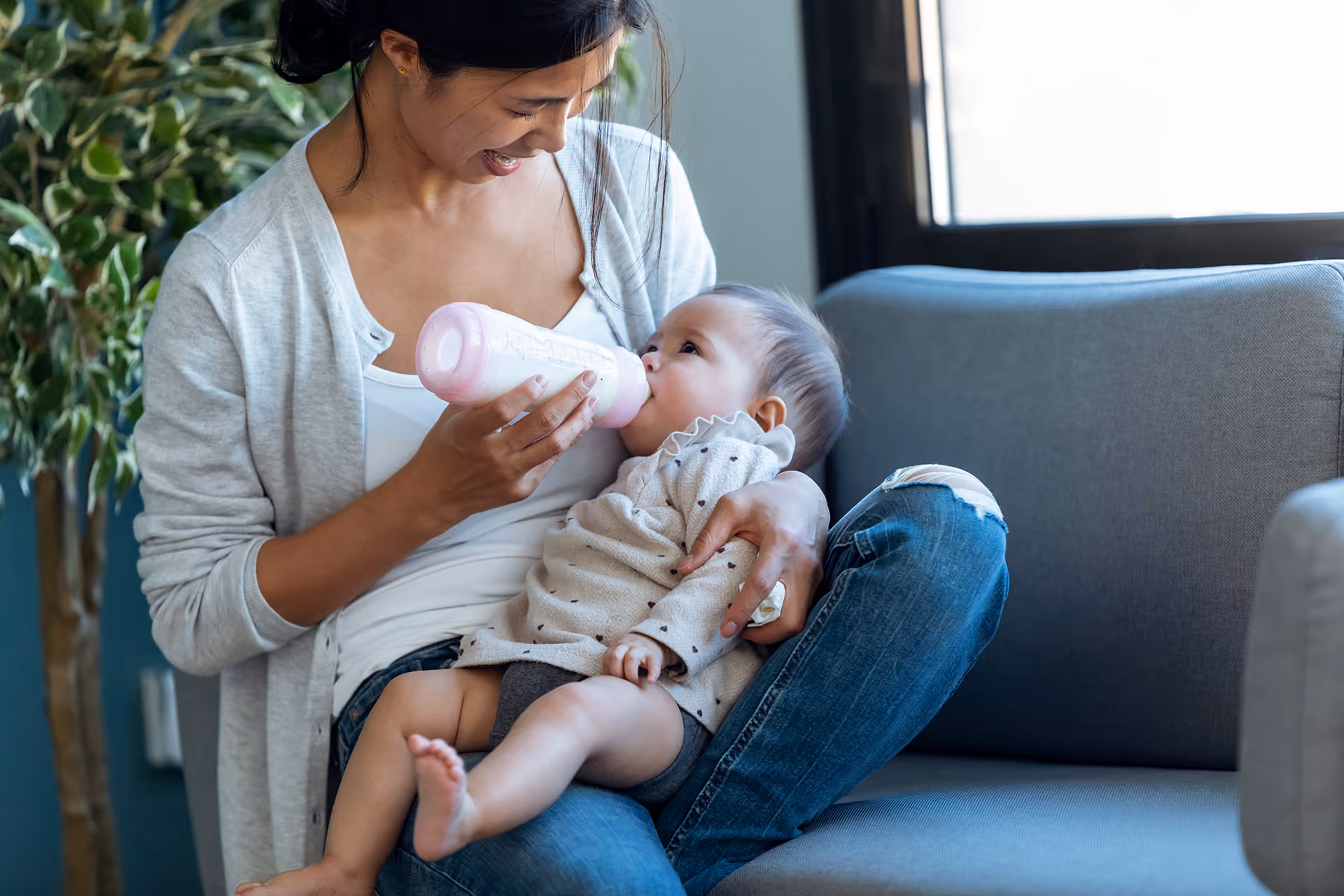 Frau gibt einem Baby auf dem Sofa das Fläschchen