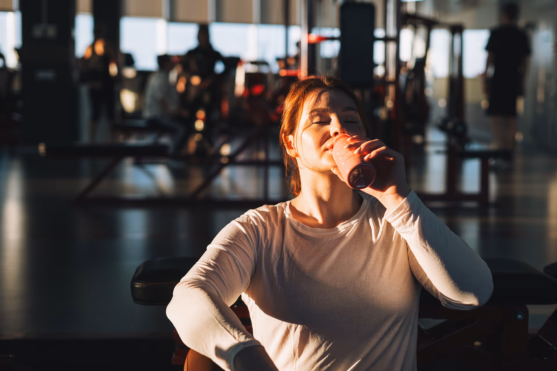 Frau im Fitnessstudio trinkt mit geschlossenen Augen ein rotes Sportgetränk aus einer Flasche [no AI]
