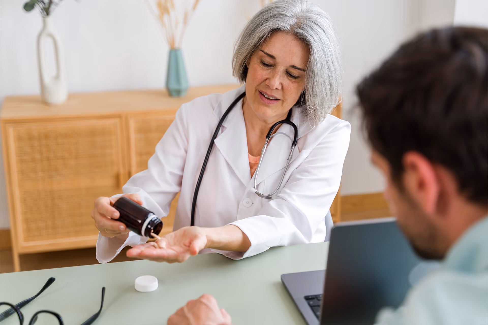 Ärztin mit Stethoskop schüttet vor einem Patienten Tabletten aus einer Flasche in ihre Hand [no AI]