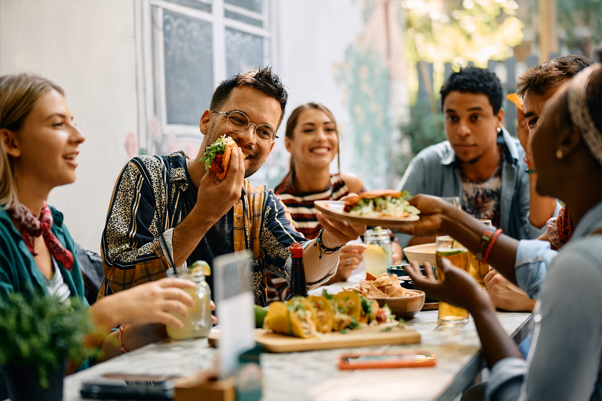 Freundesgruppe teilt Tacos und kalte Getränke an einem Restauranttisch im Freien [no AI]