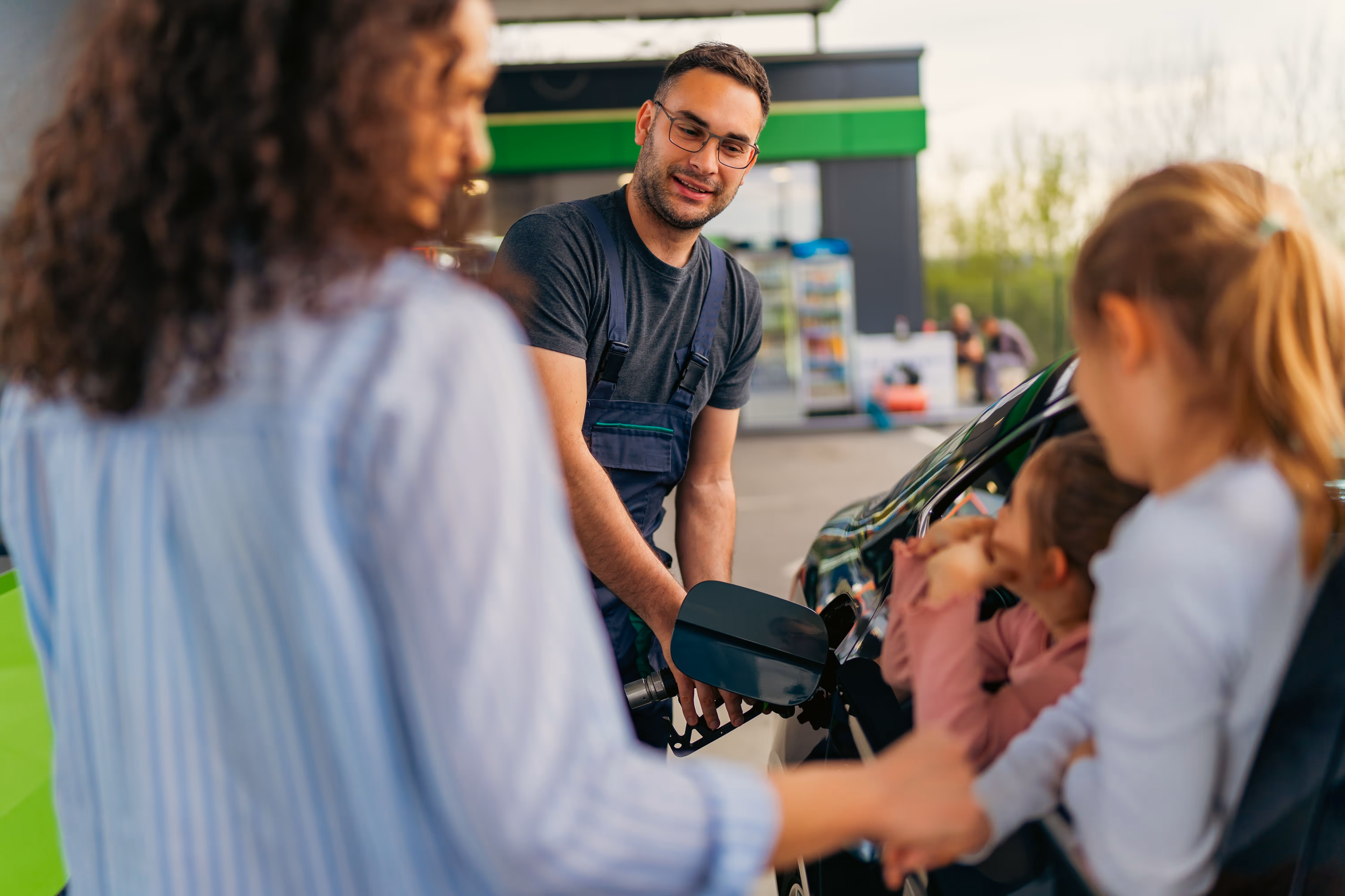Tankwart betankt ein Auto, während eine Mutter mit zwei Kindern wartet