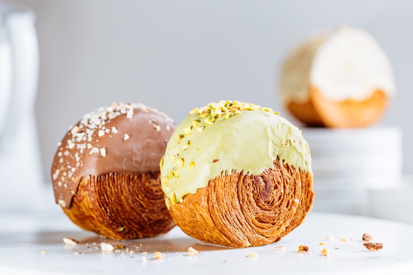 Runde Croissant-Gebäckstücke mit Schokoladen- und Pistazienglasur, bestreut mit gehackten Nüssen