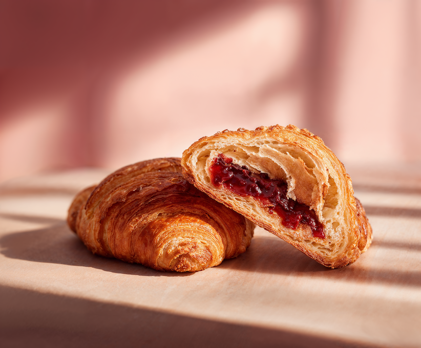 Aufgeschnittenes Croissant mit roter Fruchtfüllung, dahinter ein ganzes Croissant