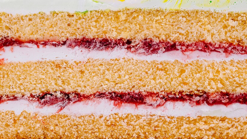 Querschnitt eines Biskuitkuchens mit Schichten aus Creme und roter Fruchtfüllung