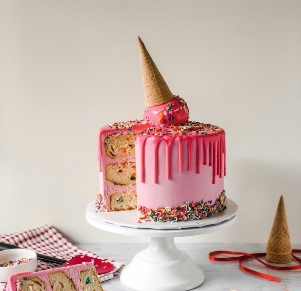 Rosa Schichttorte mit tropfender Glasur, Streuseln und einem umgedrehten Eistütchen obenauf