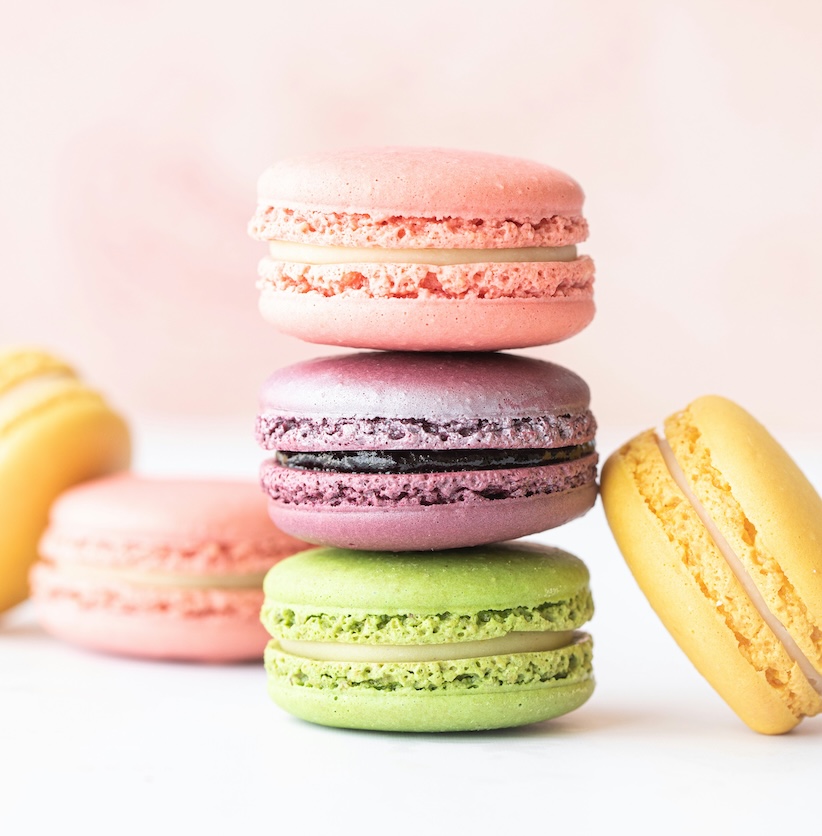 Stapel aus rosa, violetten und grünen Macarons, daneben gelbe Macarons