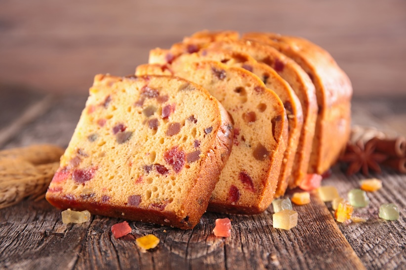 Aufgeschnittener Früchtekuchen mit kandierten Fruchtstücken auf rustikalem Holzbrett